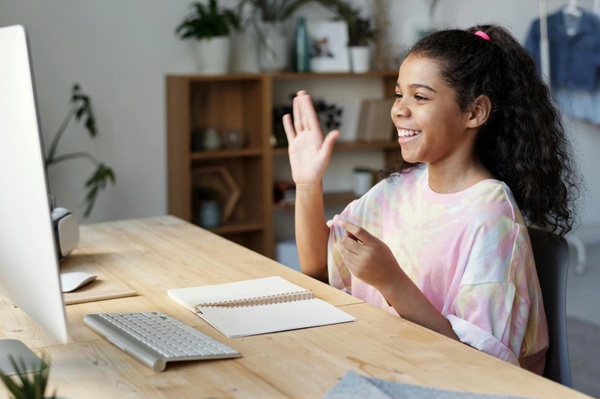 A girl waving at a computer screen during an online lesson