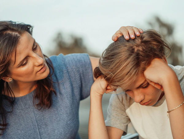 A parent comforting an upset teenager who is holding their head in their hands