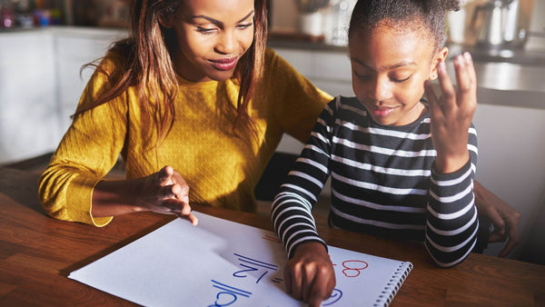 A parent and child working through a workbook together at a table