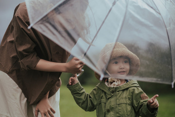 A parent crouching under an umbrella with a young child in the rain