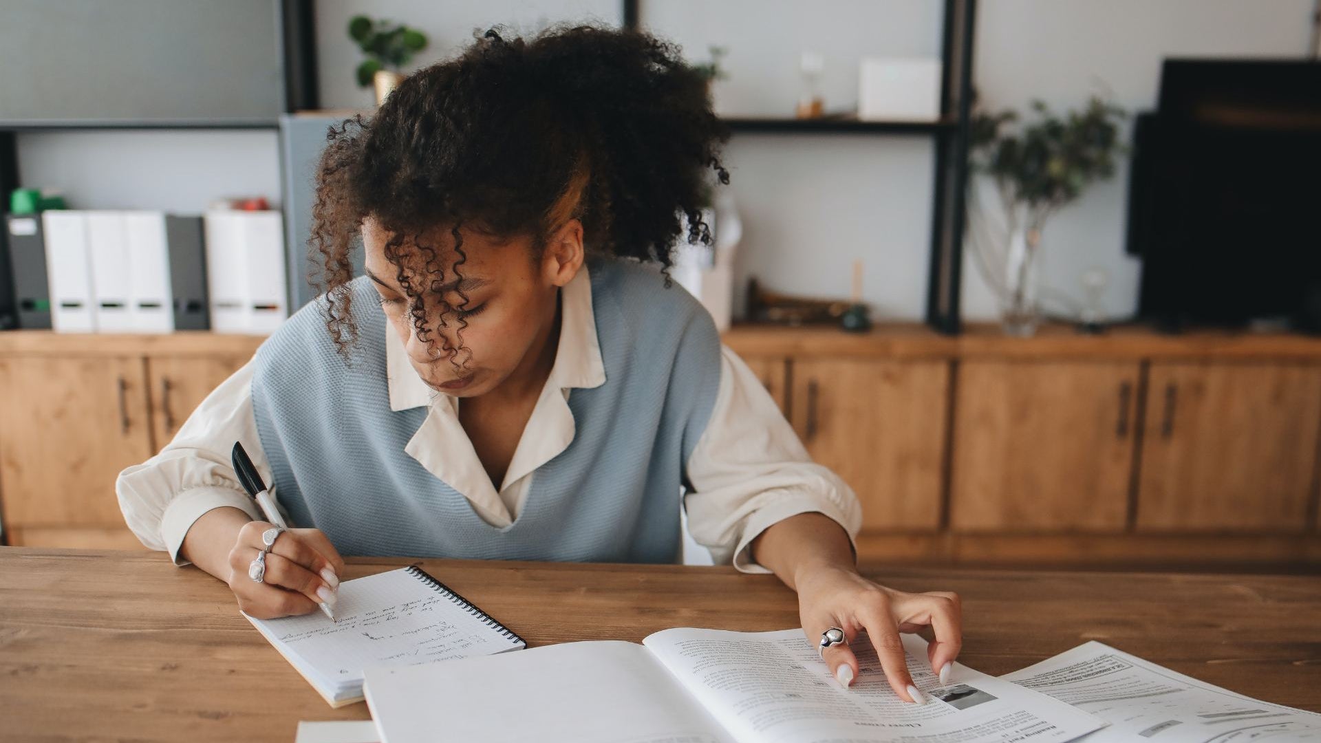 Focused student studying at home, writing notes while referencing GCSE textbooks. Represents dedication to learning and academic success through personalised online tutoring support.